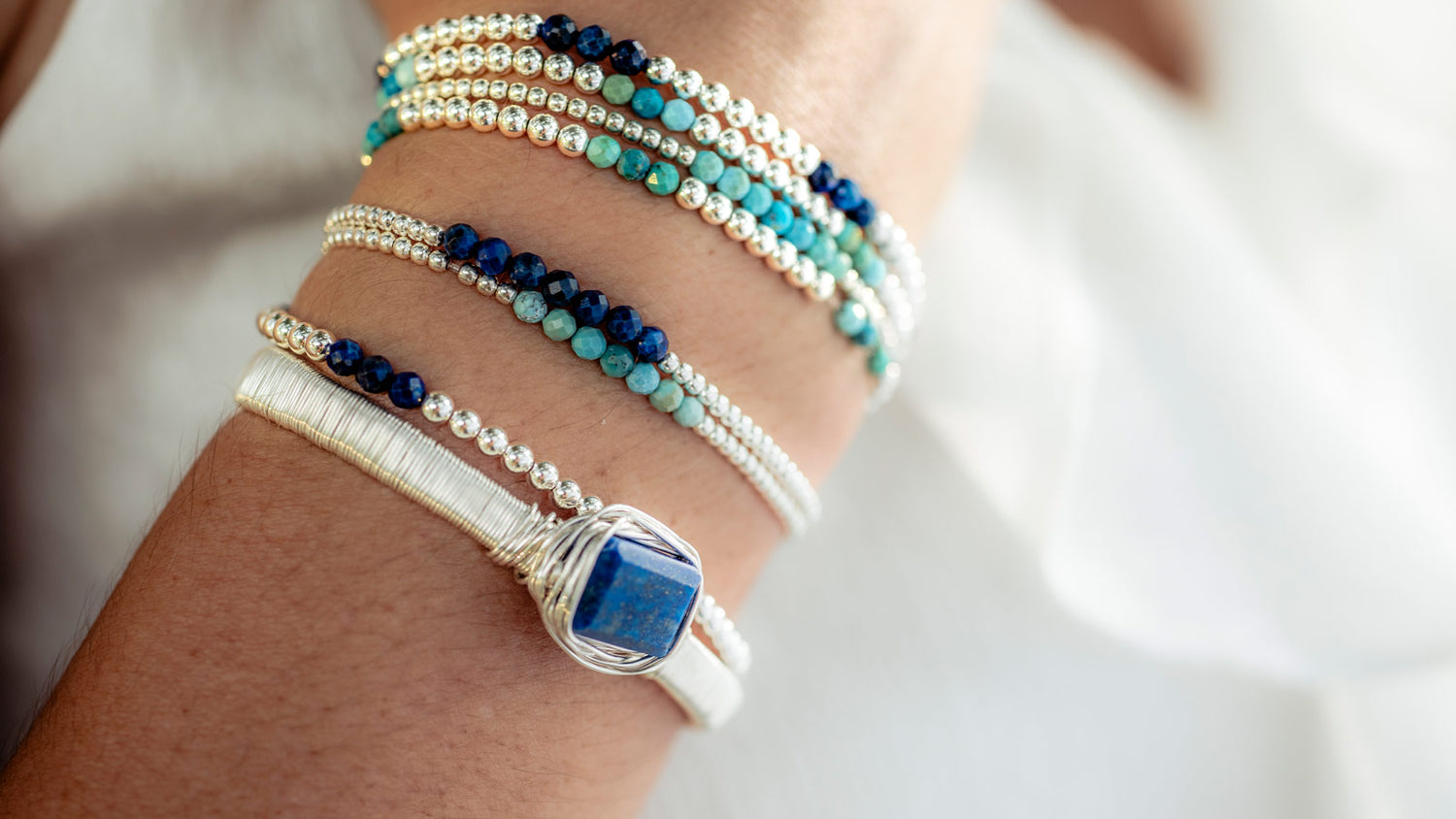 Close-up of a wrist wearing multiple beaded bracelets with a whitebackground