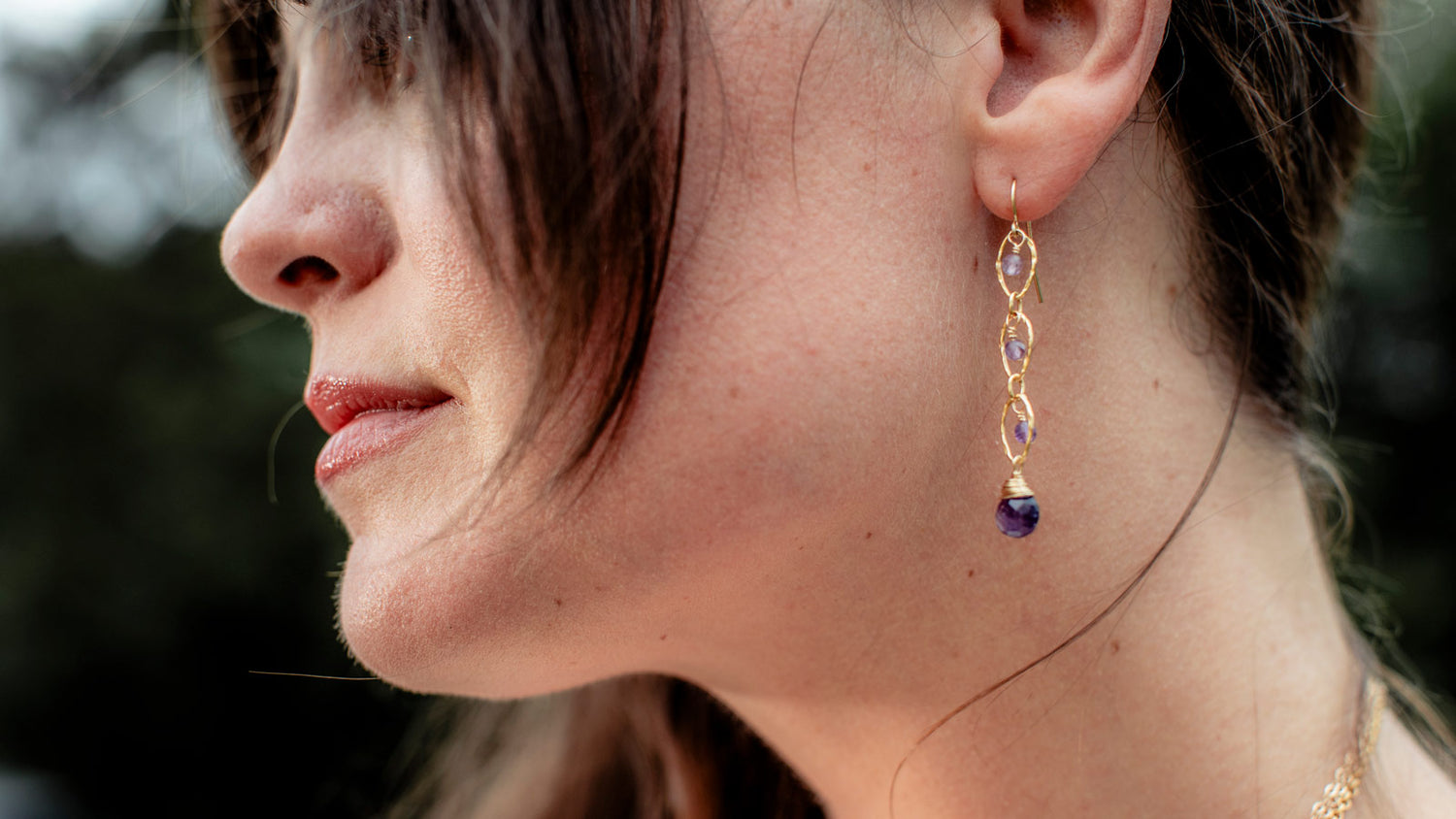 Close-up of a woman wearing gold earrings with purple gemstones.