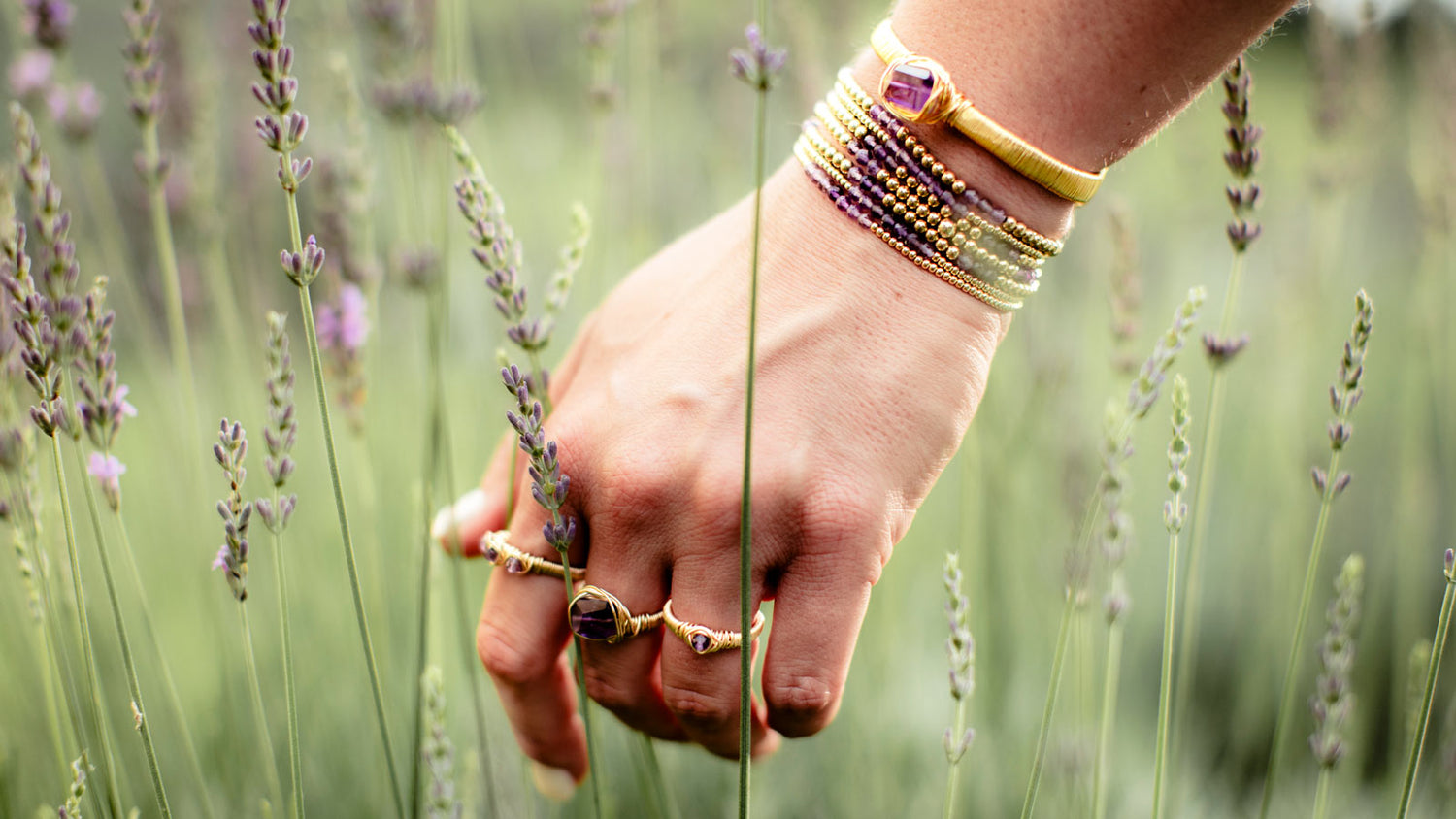 14k gold filled rings and bracelets holding lavender flowers in a field